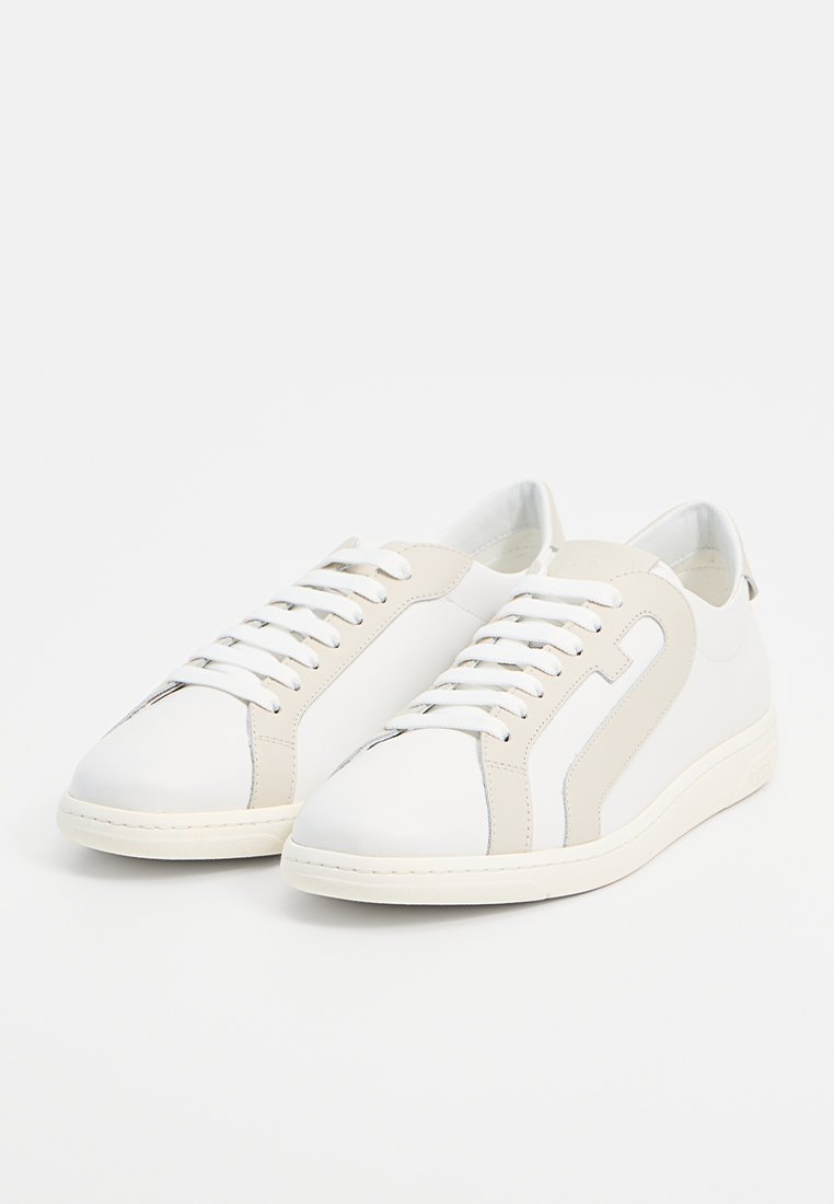 Para niskich białych sneakersów z beżowymi akcentami, białymi sznurowadłami i gumowymi podeszwami, sfotografowana na białym tle.