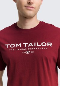 Bordeauxkleurig katoenen t-shirt met ronde hals, met prominente witte tekst: "TOM TAILOR THE CASUAL DEPARTMENT 1962".