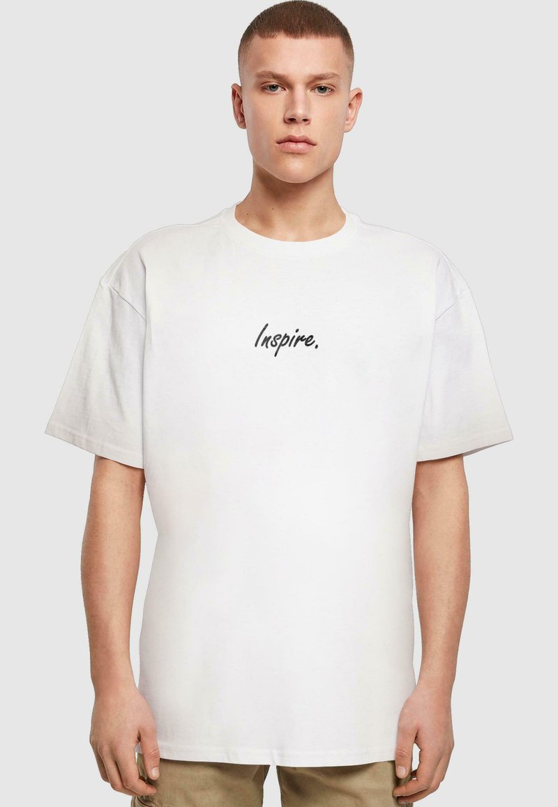 Fehér, rövid ujjú póló, középen fekete, dőlt betűkkel írva: "Inspire." Puha pamutból készült, laza szabással.