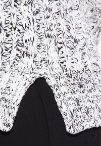 Gestickter Pullover in Schwarz und Weiß, der ein strukturiertes Zickzackmuster aufweist. Er hat einen geteilten Saum und ist aus dickem Garn gefertigt.
