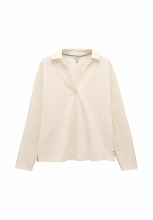 Krémová košeľa s dlhým rukávom, otvoreným golierom a jemne textúrovanou látkou, s malými rozparkom na bočných stranách lemu a slabým logom na ľavej hrudi.