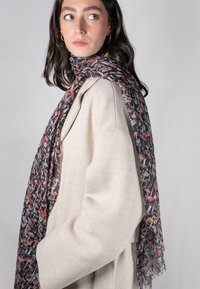Sciarpa leggera con una base nera, caratterizzata da un motivo di funghi colorati in rosso, rosa e verde. I bordi sono leggermente frangiati.
