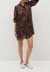 Vestido negro de flores con mangas largas, cuello y un corte holgado. Presenta intrincados patrones rojos y dorados, tela semitransparente y un dobladillo corto.