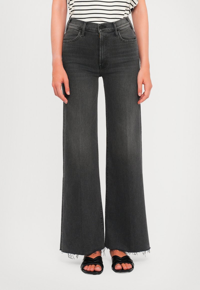 Wide-leg black denim jeans with a raw hem, high waist, and slight fading. Paired with black slide sandals and a striped top.