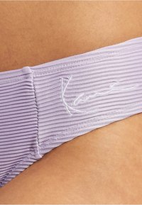 Levandi ribbelt bikini alsó, rugalmas derékkal, fehér hímzett logóval. Puha tapintású, látható varrási részletekkel.