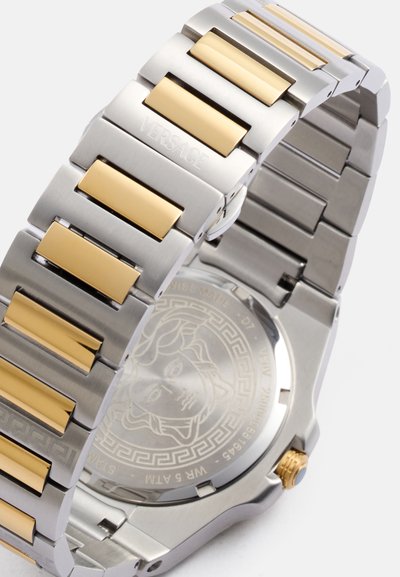 Orologio in acciaio inossidabile con bracciale a maglie in tonalità argento e oro; presenta una lunetta decorata e un fondello trasparente con un design a Medusa.