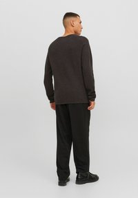 Donkergrijze lange mouwen shirt met een ronde hals, gecombineerd met zwarte broeken en zwarte schoenen. Glad textuur, casual pasvorm.