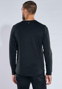 Schwarzes Langarmshirt aus weichem Material, mit rundem Ausschnitt und dezentem Akzentdetail am Nacken.