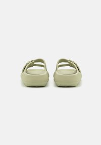 Svijetlozelene slip-on sandale s teksturiranom potplatom, s dvostrukim trakama i cvjetnim naglaskom sa strane. Ravnog i zaobljenog oblika.