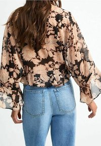 Blouse en dentelle florale avec de longues manches volantes en noir et pêche, associée à un jean taille haute bleu clair avec des poches arrière.