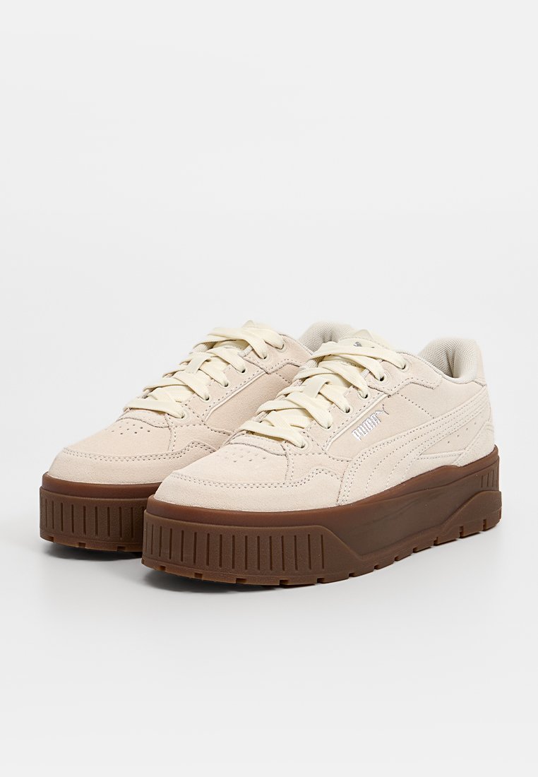 Sneakers in scamosciato beige con suola spessa marrone, lacci piatti e perforazioni sottili. Presentano il marchio sul lato e un design testurizzato.