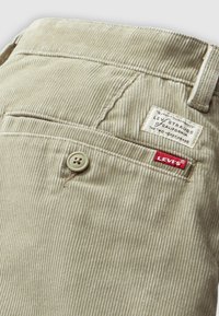 Beige corduroy Levi's pants pocket with button and brand labels, showing fabric texture and stitching details.