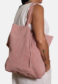 Borsa tote in suede rosa con due lunghe tracolle, design minimalista e texture morbida. Presenta un'apertura superiore con chiusura a coulisse.