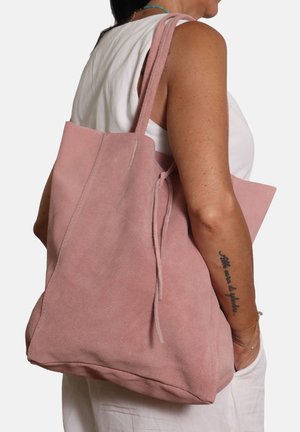 Sac fourre-tout en daim rose avec deux longues sangles, au design minimaliste et à la texture douce. Il dispose d'une ouverture supérieure avec une fermeture à cordon.