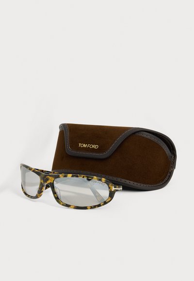 Lunettes Tom Ford à motif écaille avec verres clairs, reposant devant un étui à lunettes Tom Ford en daim marron.