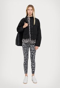 Veste noire cropped avec une fermeture éclair, haut à motif animal, et legging. Baskets blanches, cheveux lisses, et un sac fourre-tout noir complètent le look.