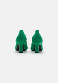 Scarpe con tacco alto in suede verde con punta affilata e tacco nero stretto, caratterizzate da una texture liscia e un design minimalista.