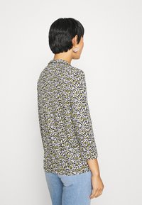 Blusa fluida con un motivo floreale scuro in verde, giallo e bianco. Presenta un colletto e maniche a trequarti. Tessuto morbido.