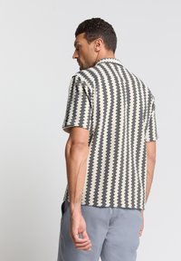 Korte mouwen shirt in crème met zwart zigzagpatroon, met een kraag, ontspannen pasvorm en textuurstof.