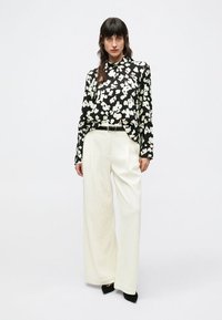 Černobílá květovaná halenka s dlouhými rukávy, doplněná o bílé kalhoty s vysokým pasem a širokými nohavicemi, texturovaná látka a černé lodičky.