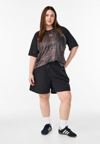 Pantalones cortos deportivos negros combinados con una camiseta de estampado de leopardo holgada. Tejido suave, mangas cortas, cintura con cordón y zapatillas deportivas.
