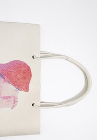 Beige gestructureerde leren tote bag met een abstract ontwerp in roze en paars, voorzien van twee ronde handvatten en een eenvoudige, open-top structuur.