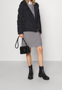 Chaqueta acolchada negra con capucha, vestido gris ajustado, bolsa negra con correa y botas negras con suelas gruesas. Texturas suaves, diseño minimalista.