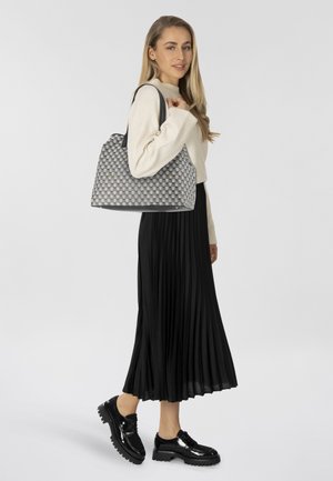 Borsa a tracolla grigia intrecciata con motivo a scacchi, manici in pelle nera e finitura opaca. Il modello indossa una gonna nera plissettata e scarpe verniciate.