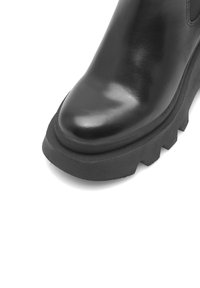 Černá kožená kotníková bota s kulatou špičkou, texturovaným bokem a silnou gumovou podrážkou s výrazným vzorem.