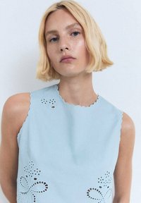Top senza maniche azzurro chiaro con scollatura a scallop, dotato di ricami floreali a intaglio sulla parte anteriore. Tessuto dalla texture liscia.