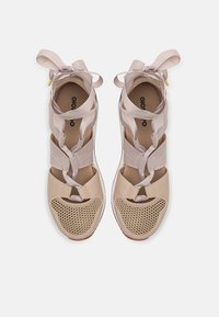 Zapatillas beige con parte frontal de malla, correas superpuestas y lazadas de cinta; cuentan con una puntera redondeada y suela texturizada para mayor agarre.