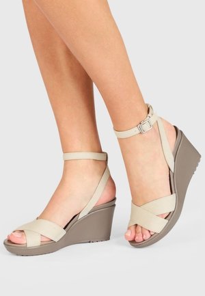 Sandales compensées beiges avec un design de bride texturée, une bride de cheville ajustable et une semelle plateforme solide gris foncé.