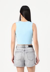 Ανοιχτό μπλε, χωρίς μανίκια, κοντό τοπ με στρογγυλή λαιμόκοψη. Συνδυάζεται με γκρι τζιν σορτς που διαθέτουν διπλωμένα μανίκια και δύο πίσω τσέπες.