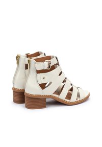 Botines de cuero blanco con diseño recortado, hebilla ajustable y herrajes dorados. Con tacón marrón apilado y forro en contraste.