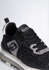 Svarta glittrande sneakers med texturerad ovandel, svarta snören och kontrasterande vit sula. Har en logotypdetalj och vadderad krage för komfort.
