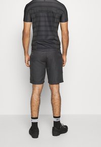 Camisa negra de manga corta con un patrón a rayas, combinada con pantalones cortos gris oscuro. El conjunto incluye calzado negro y calcetines hasta el tobillo.