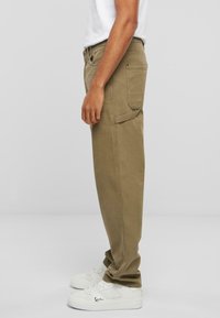 Pantalons cargo kaki avec coupe droite, deux poches latérales et une poche arrière supplémentaire, associés à des baskets blanches.