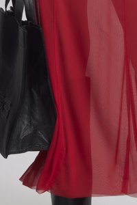 Raudona permatoma medžiaga elegantiškai krenta, derinama su juodu odiniu rankiniu krepšiu, turinčiu lygią tekstūrą ir išsamų siuvinėjimą.