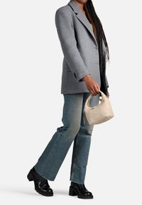 Borsa di pelle liscia color beige chiaro con manici corti. Indossata con un blazer grigio, jeans in denim con finitura sbiadita e stivali neri con tacco.