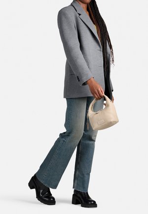 Borsa di pelle liscia color beige chiaro con manici corti. Indossata con un blazer grigio, jeans in denim con finitura sbiadita e stivali neri con tacco.