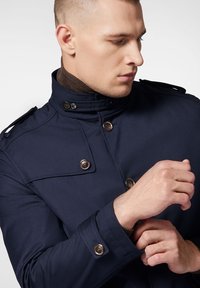 Granatowa kurtka z gładkiego materiału, z wysokim kołnierzem, podwójnym zapięciem na duże mosiężne guziki oraz pagonami na ramionach.