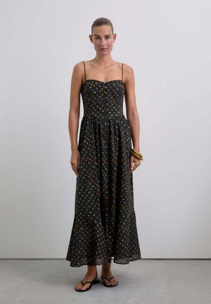 Vestido maxi negro sin mangas con un corpiño ajustado, falda acampanada y un patrón geométrico multicolor; combinado con sandalias negras minimalistas.