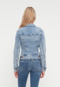 Svetlo modra denim jakna z oprijetim dizajnom, koničastim ovratnikom in dolgimi rokavi. Ima šivi in žepke na hrbtni strani.