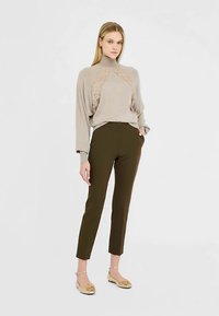Beige turtleneck sweater with lace detailing, paired with olive green fitted trousers. The model wears gold flats with a bow accent.