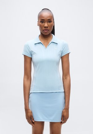 Világoskék atlétikai galléros póló V-nyakkal, rövid ujjal és bordázott textúrával, hozzá illő, testhez simuló szoknyanadrággal. Logó a mellkason.