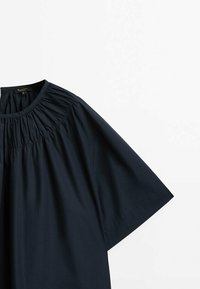 Top blu navy a maniche corte con scollatura arricciata. Realizzato in tessuto morbido, presenta una vestibilità comoda e una leggera texture. Design minimale.