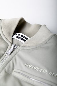 Heledhalli bombersaadiga, millel on sile tekstuur, varustatud tõmblukuga ja soonikkraega. Rinna kohal on tikitud "COLOURFUL REBEL" bränding.