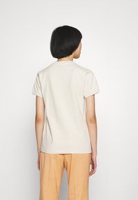 Camiseta de algodón beige con mangas cortas y cuello redondo, combinada con pantalones de cuadros a rayas naranja claro, vista desde la parte posterior.