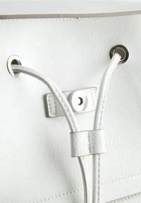 Sac en cuir blanc avec des cordons coulissants passés à travers des œillets métalliques et sécurisé par une fermeture magnétique.