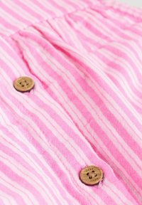 Pink and white striped fabric with a textured finish. Features wooden buttons. The design includes gathered sections and vertical lines.